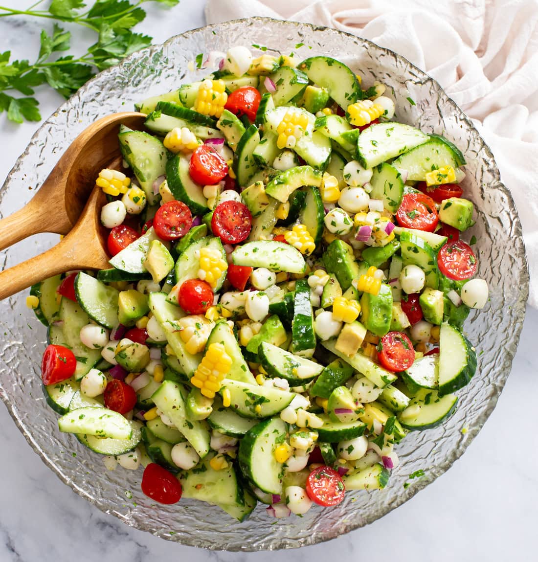 Cucumber Avocado Salad in a glass bowl with salad tongs on the side.