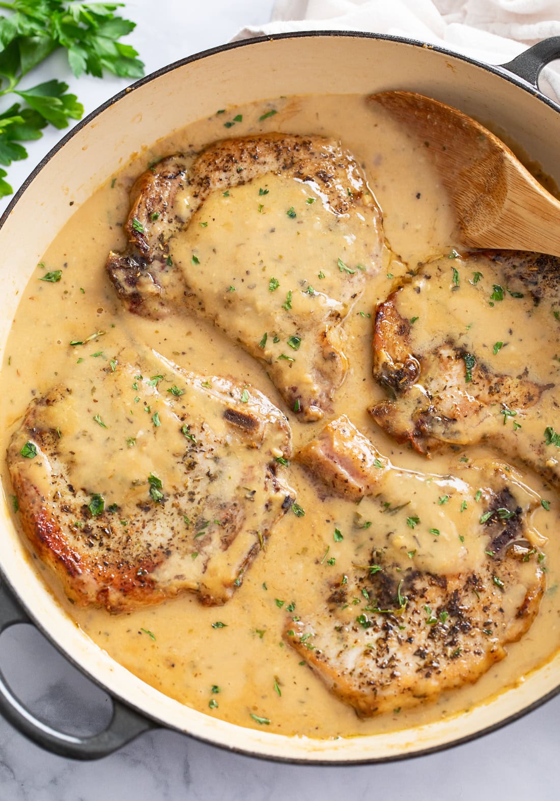 Garlic Parmesan Pork Chops in a skillet with a spoon on the side and parsley on top.