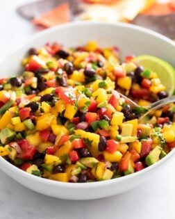 Mango Salsa in a white bowl with a spoon scooping it up.