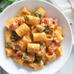 Creamy Tomato Spinach Pasta in a white bowl with tomatoes, sausage, and spinach.