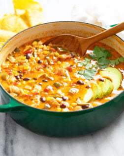 Chicken Poblano Soup in a green Dutch oven with sliced avocado on top and a spoon on the back.