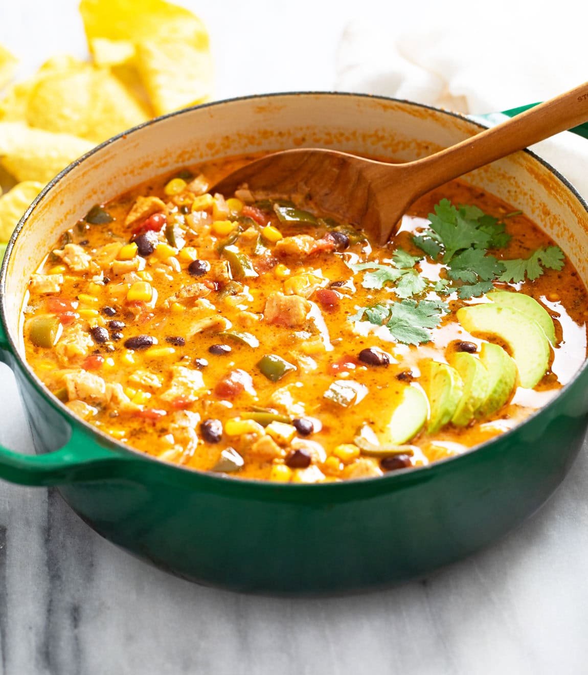 Chicken Poblano Soup in a green Dutch oven with sliced avocado on top and a spoon on the back.