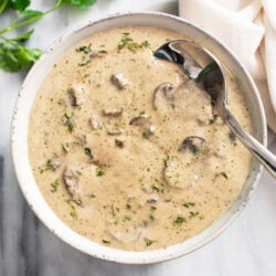 Cream of mushroom soup in a white bowl with parsley on top and a spoon on the side.