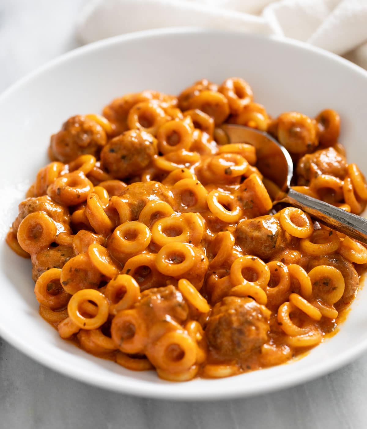 Homemade Spaghettios in a white bowl with a spoon on the side.