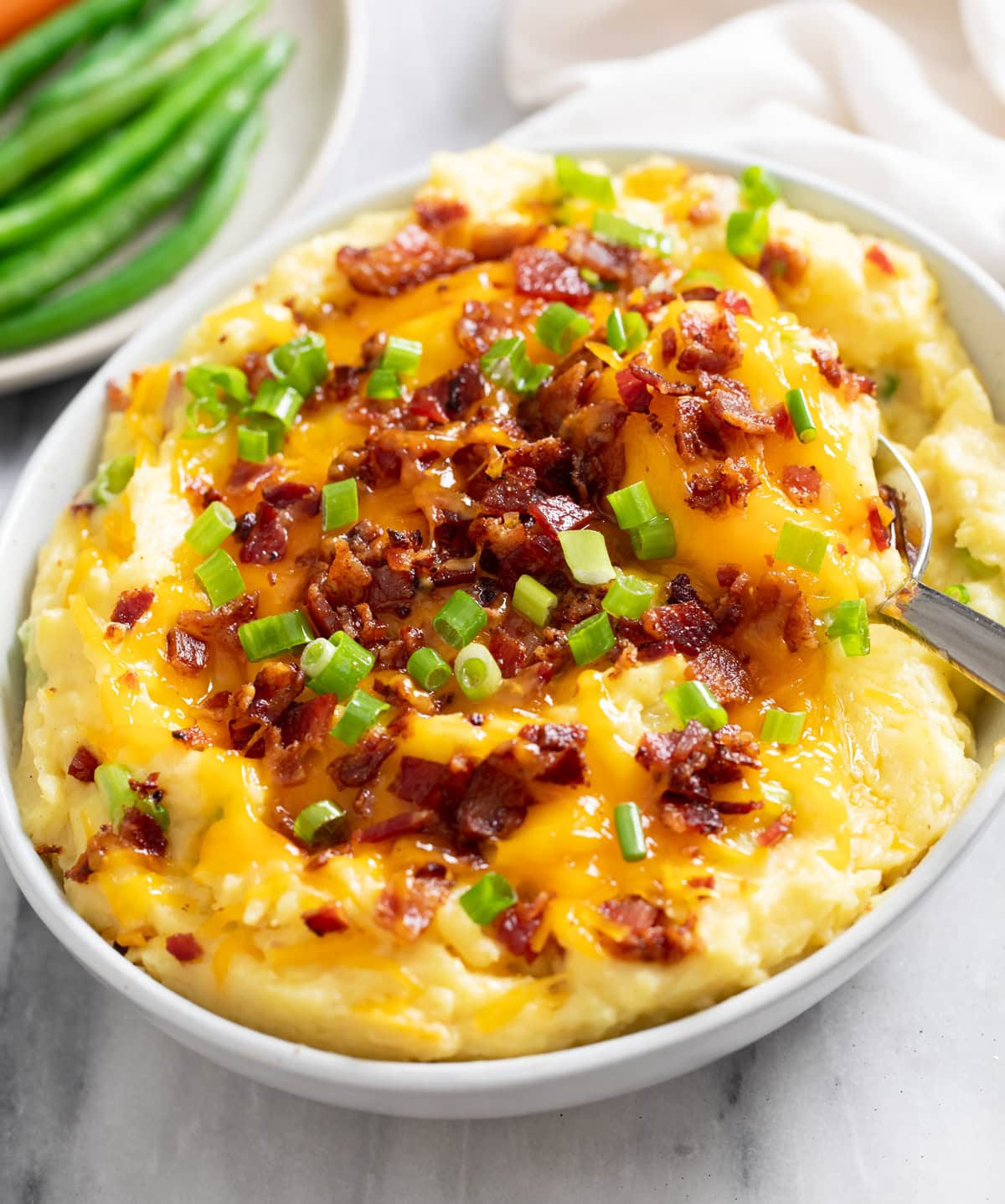 Loaded Mashed Potatoes in a white bowl with bacon, cheese, and green onions on top.