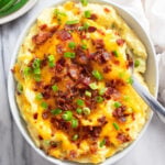 Loaded Mashed Potatoes in a white bowl with melted cheese, crispy bacon, and sliced green onions.