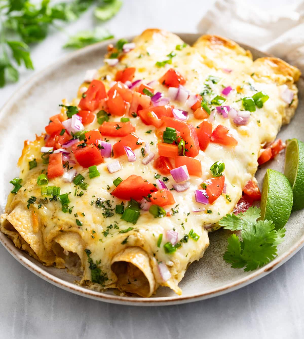 Cheesy White Chicken Enchiladas on a plate with lime wedges and cilantro on the side.