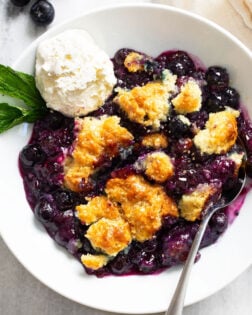 Blueberry Cobbler in a white bowl with a scoop of ice cream and sprig of mint on the side.