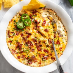 Jalapeno Popper Dip in a white baking dish with sliced jalapenos on top.