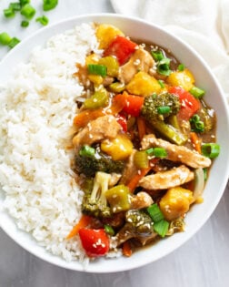 Pork Stir Fry with a brown sauce on a white plate with a bed of white rice.
