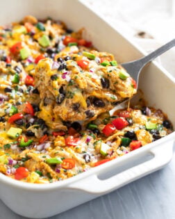 Side view of a spatula lifting out a slice of Chicken Enchilada Casserole from a white baking dish.