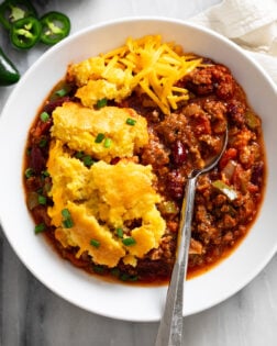 Chili Corn Casserole in a white bowl with a spoon on the side and cheese on top.