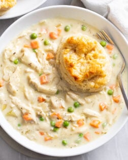 Crock Pot Chicken Pot Pie in a white bowl with a fork and a buttermilk biscuit.