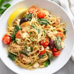 Mediterranean Pasta in a white bowl with spinach, tomatoes, chicken, feta, and olives.