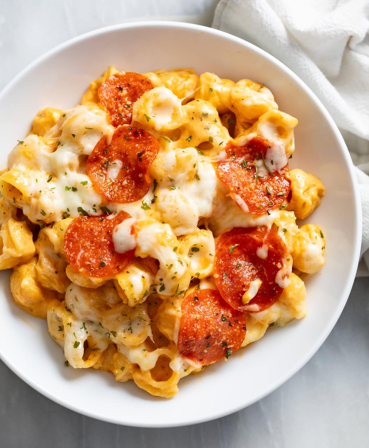 Pizza Mac and Cheese with mozzarella and pepperoni on top in a white bowl.