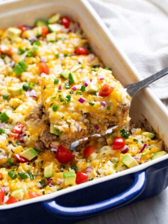 Burrito Casserole with beef, tortillas, cheese, refried beans, and rice being scooped out of a casserole dish.