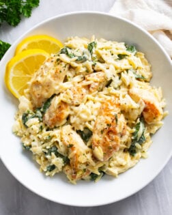 Lemon Chicken Orzo in a white bowl with lemon slices on the side and chicken and spinach in a creamy sauce with orzo.