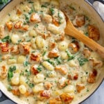 A skillet filled with Creamy Chicken Gnocchi with spinach and a wooden spoon on side.