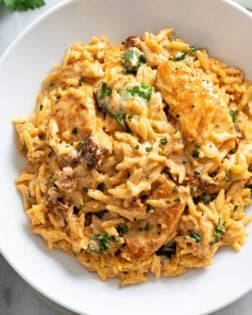 Marry Me Chicken Orzo in a creamy tomato sauce with sun-dried tomatoes and spinach in a white bowl.