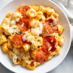 A white serving bowl filled with creamy Pizza Mac and Cheese topped with mozzarella and Pepperoni.