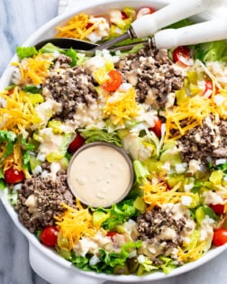 Big Mac Salad with big mac salad dressing, lettuce, ground beef, cheese, pickles, onions, and tomatoes in a white bowl.
