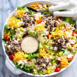 A white bowl with Big Mac Salad with big mac salad dressing, lettuce, ground beef, cheese, pickles, onions, and tomatoes.