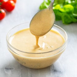 A spoon scooping Big Mac Sauce out from a glass bowl with tomatoes and lettuce in the background.