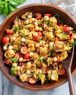 Caprese Pasta Salad in a wooden bowl with balsamic glaze drizzled on top.