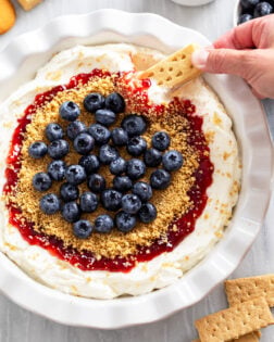 Cheesecake Dip in a pie pan with strawberry jam, graham cracker crumbs, and blueberries on top.