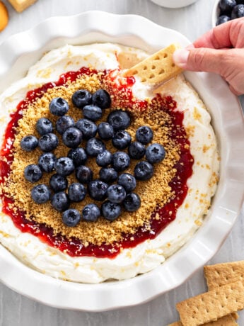 Cheesecake Dip in a pie pan with strawberry jam, graham cracker crumbs, and blueberries on top.