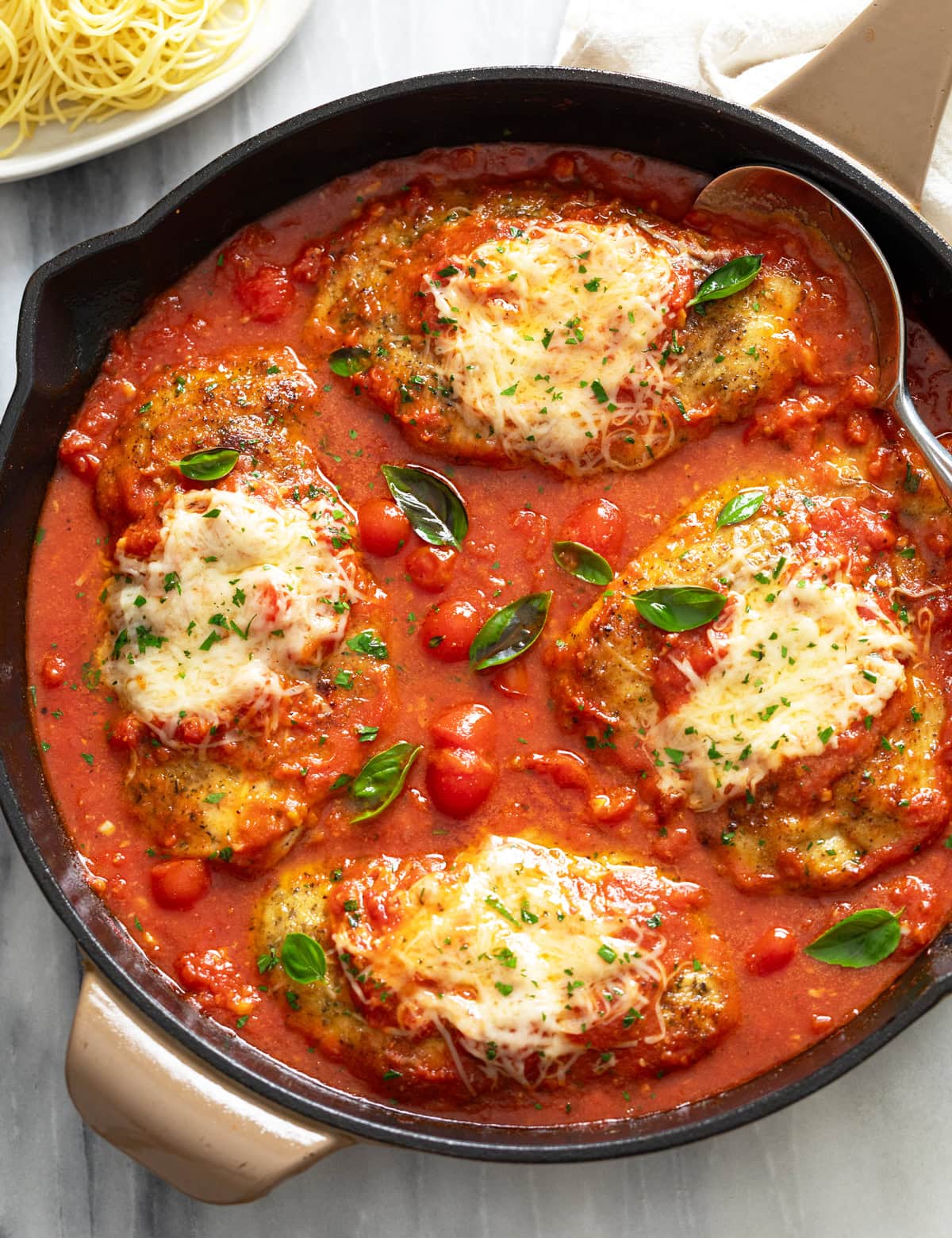Chicken Pomodoro in a black skillet with fresh tomato sauce, parmesan cheese on top, and fresh basil.