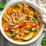 Thai Chicken Soup with noodles, chicken, and vegetables in an orange broth with garnishes.