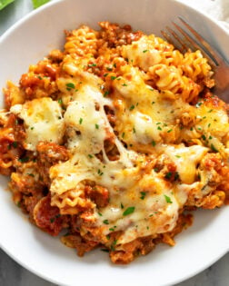Lazy Lasagna in a white bowl with melted mozzarella cheese and parsley on top and a fork on the side.